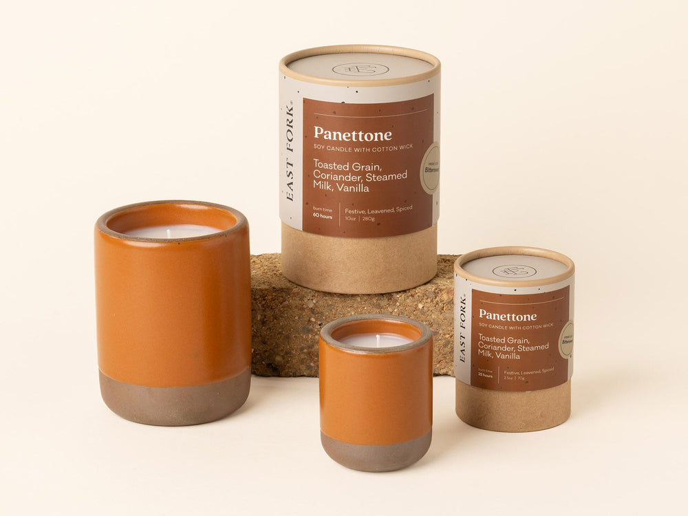 Small and large ceramic vessels in an earthy orange color with candle inside each with packaging.