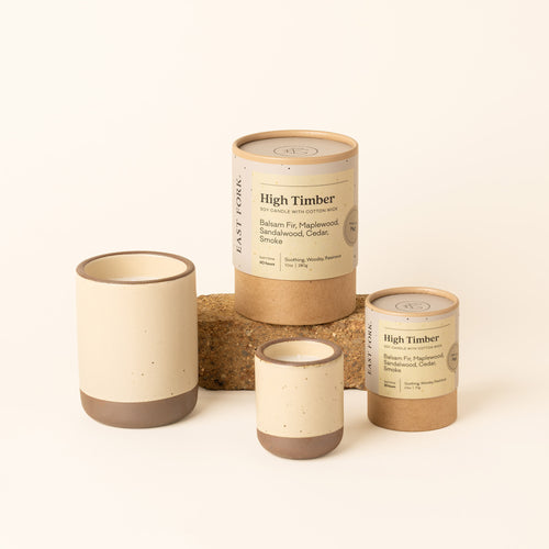 Small and large ceramic vessels in a cream color with candle inside each with packaging.