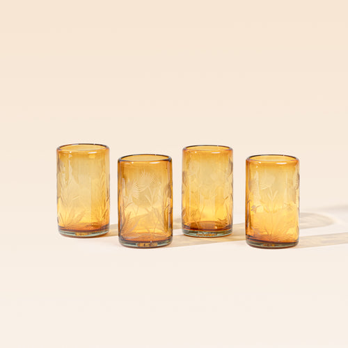 Four amber tumbler glasses made of recycled glass with etched thistle designs on it