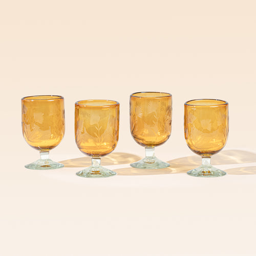 Four amber short wine glasses made of recycled glass with etched thistle designs on it