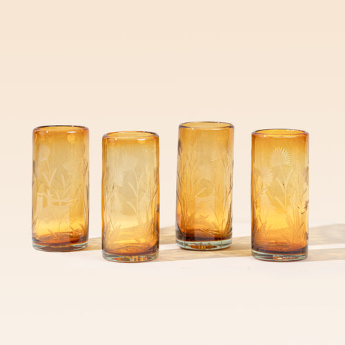Four amber cylindrical glasses with delicate etched floral pattern, standing upright on a neutral background.