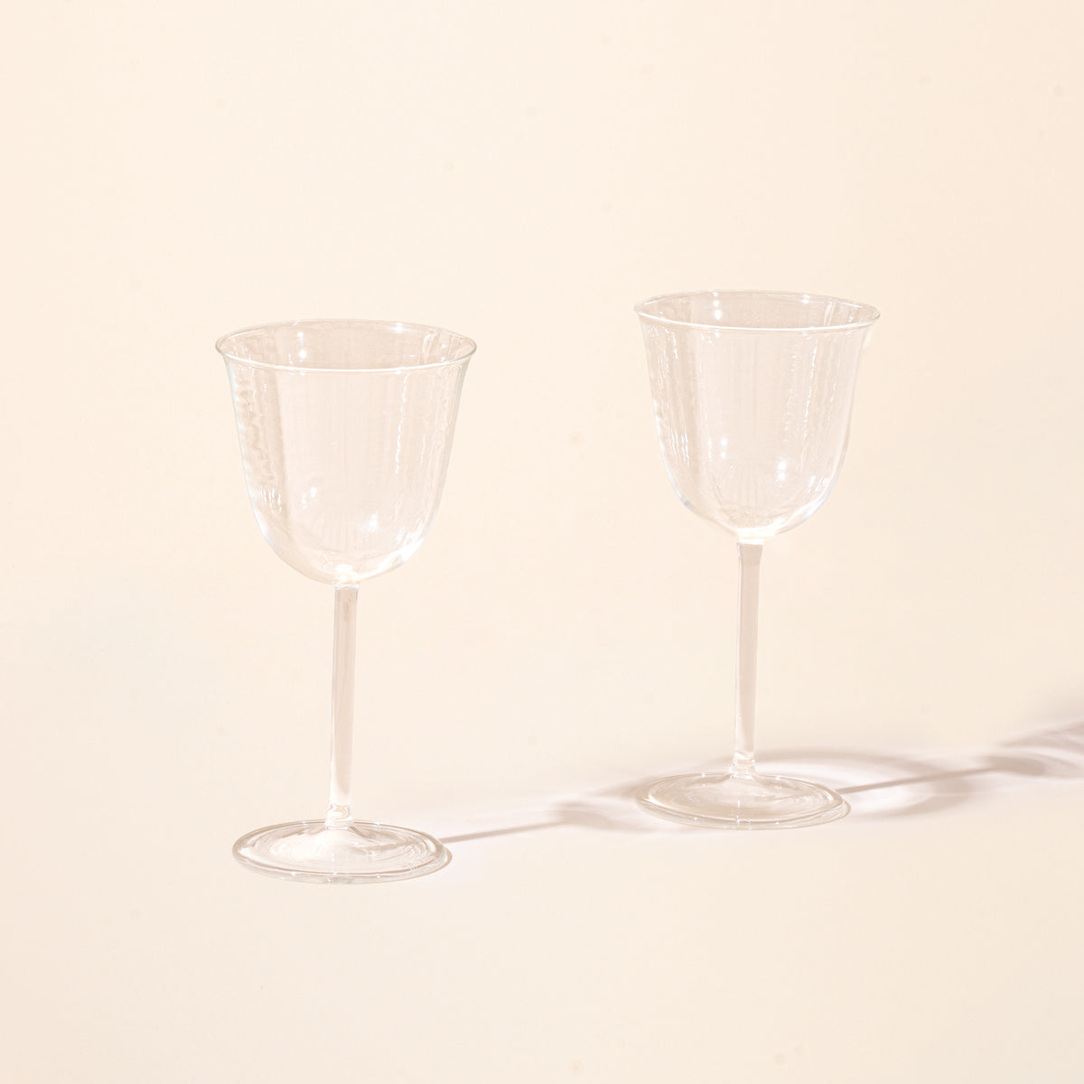 Two empty clear stemmed wine glasses on a light background.