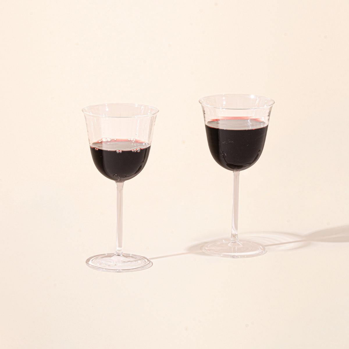 Two clear stemmed wine glasses filled with red wine on a light background.