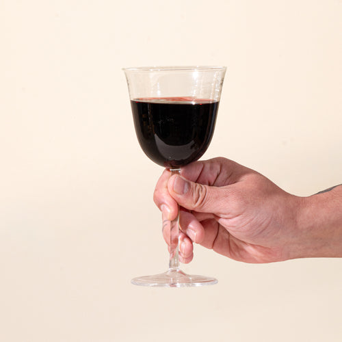 A hand holds out a clear stemmed wine glasses filled with red wine