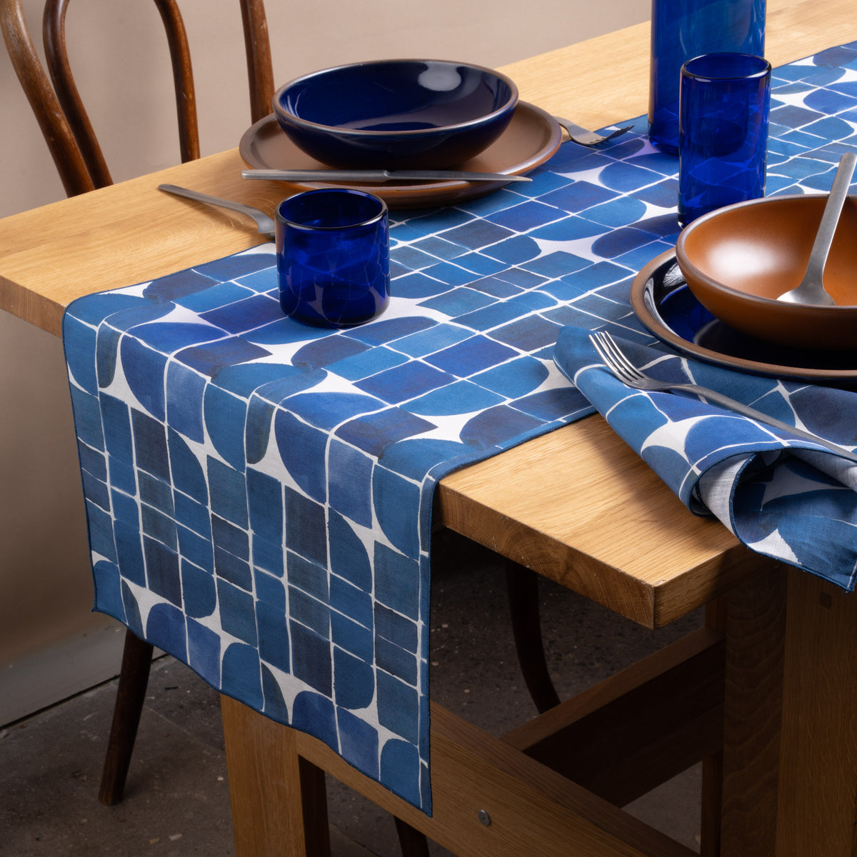 Blue geometric table runner and matching napkins styled with cobalt glassware, navy and warm brown dinnerware on a wood table.