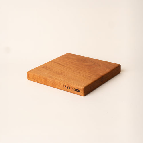 A square cherry cutting board on its side with an engraving on the edge that reads 'East Fork'
