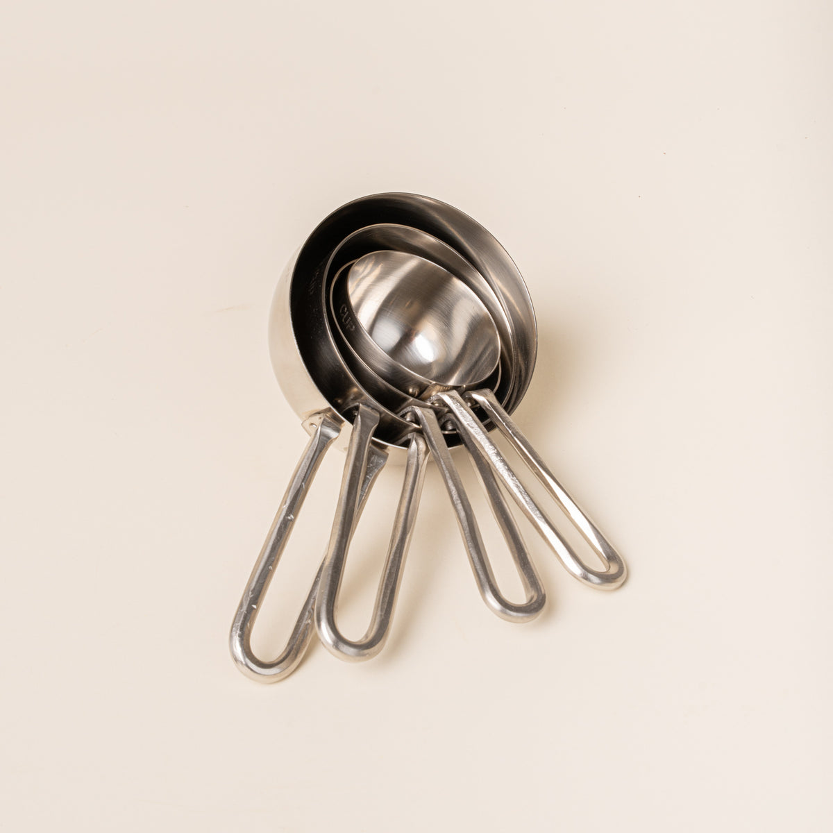 Nestled four forged measuring cups in graduated sizes, on a warm cream background.