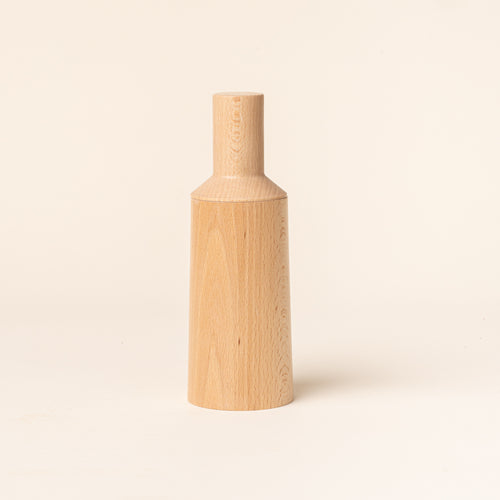 A tall cylindrical sculptural salt and pepper grinder in a natural wood on a light background.
