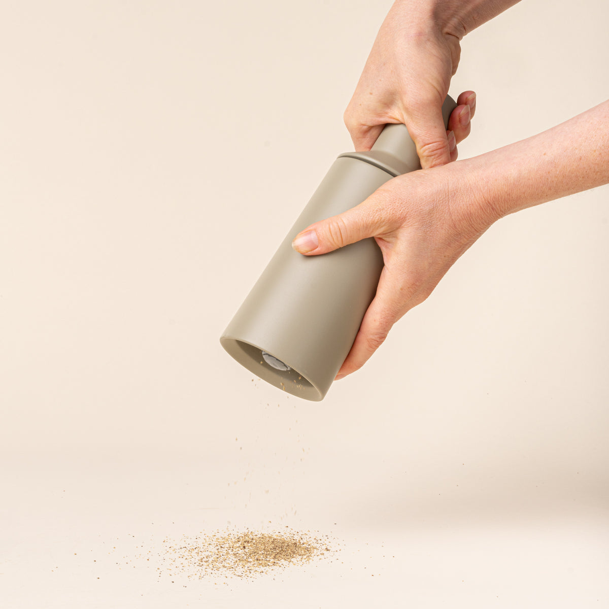 A hand holds out a tall cylindrical sculptural salt and pepper grinder in a muted light green on a light background, milling salt