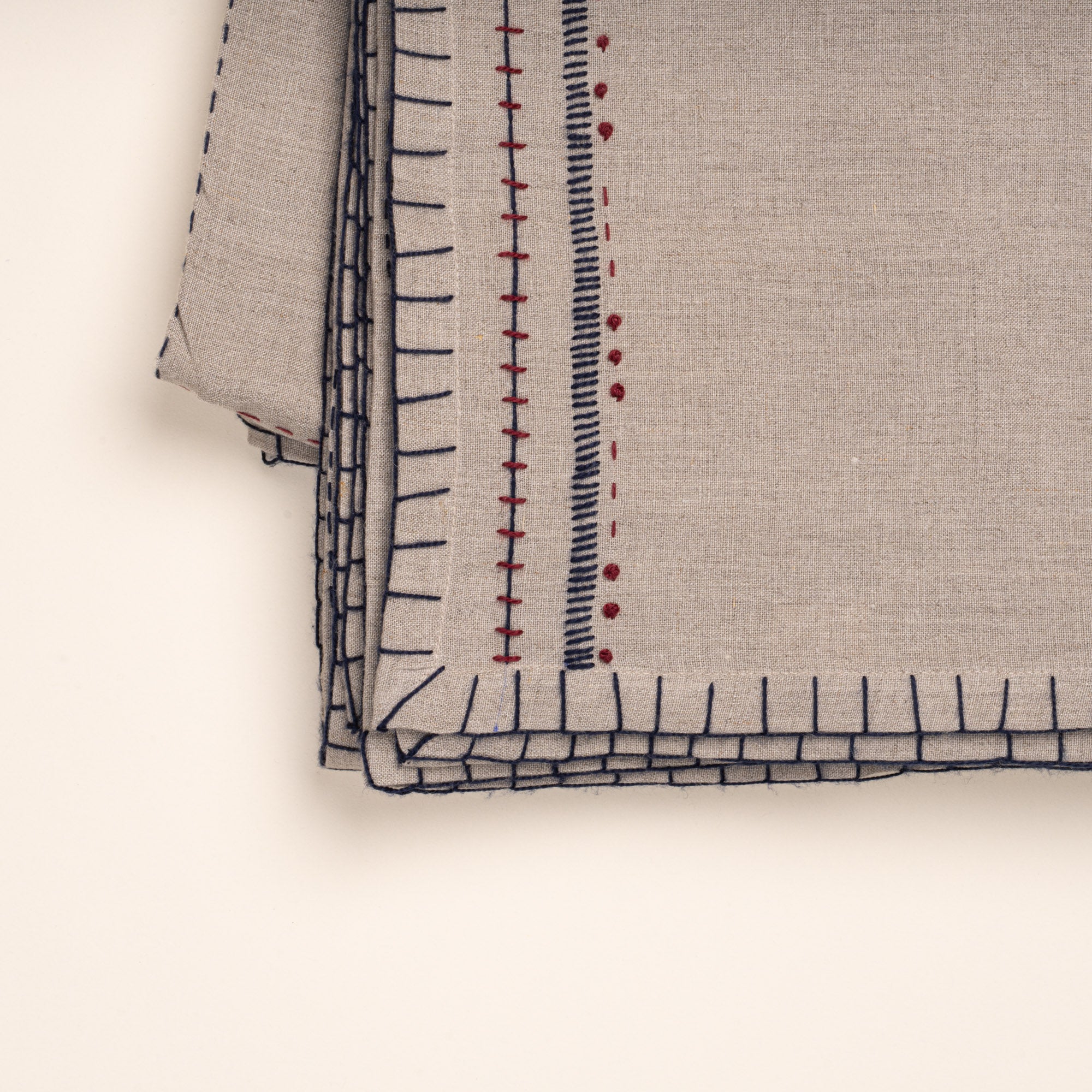 Closeup of folded natural linen tablecloth with hand-stitched navy and rust detailing and a decorative geometric border.