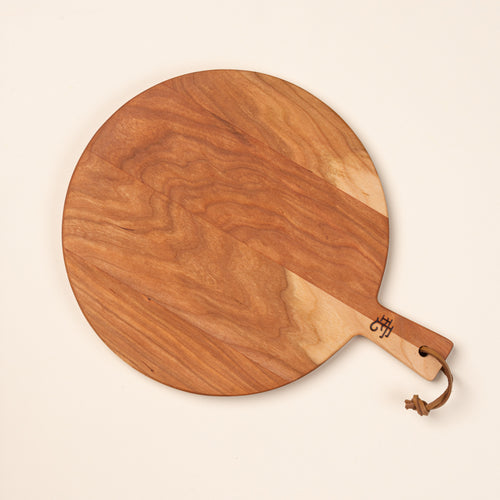 A small round cherry serving board with a short handle and leather hanging loop.