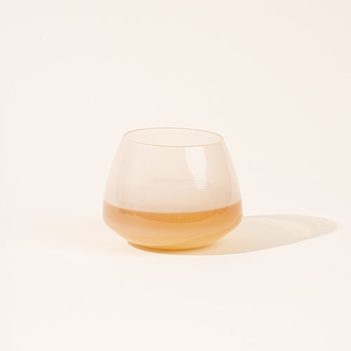 A rounded clear cream-colored glass with a warm amber-colored liquid, against a light neutral background.