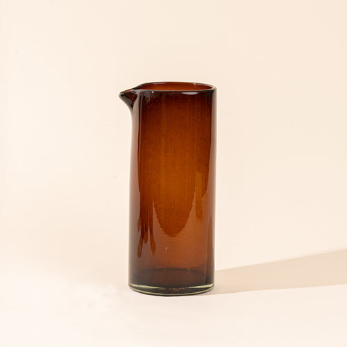 A dark amber tall transparent glass pitcher with small spout at the top