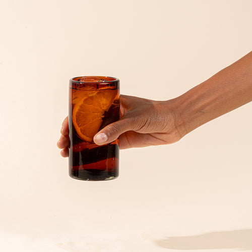 A dark amber tall transparent drinking glass with a drink and lemon slice.
