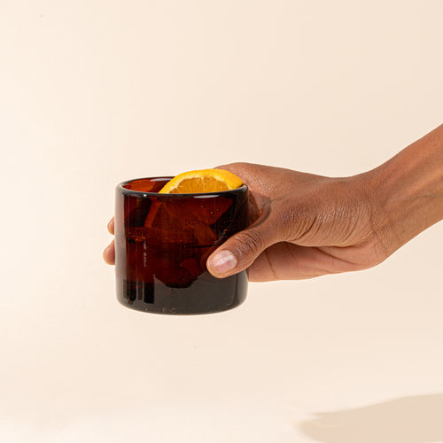 A dark amber short transparent drinking glass with a drink and lemon slice.