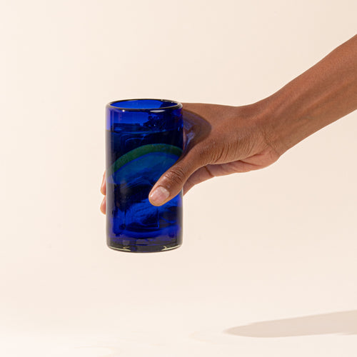A cobalt blue tall transparent drinking glass with a drink and lemon slice.
