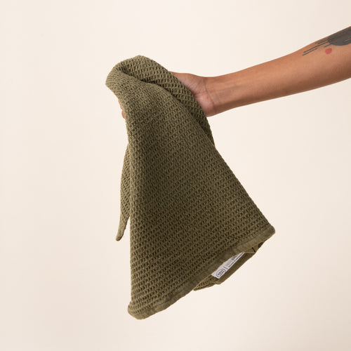 Hand holding an olive green waffle weave kitchen towel