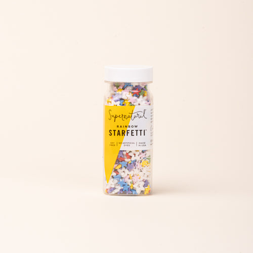 Bottle of colorful star-shaped sprinkles on a light background.