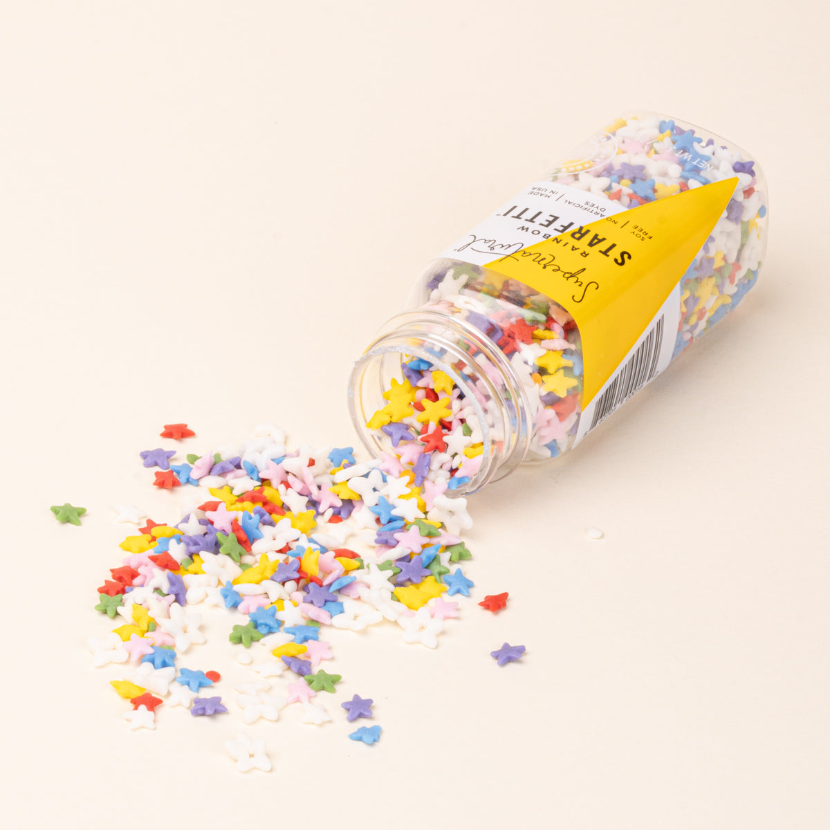 Bottle of colorful star-shaped sprinkles on a light background, on its side with sprinkles pouring out.