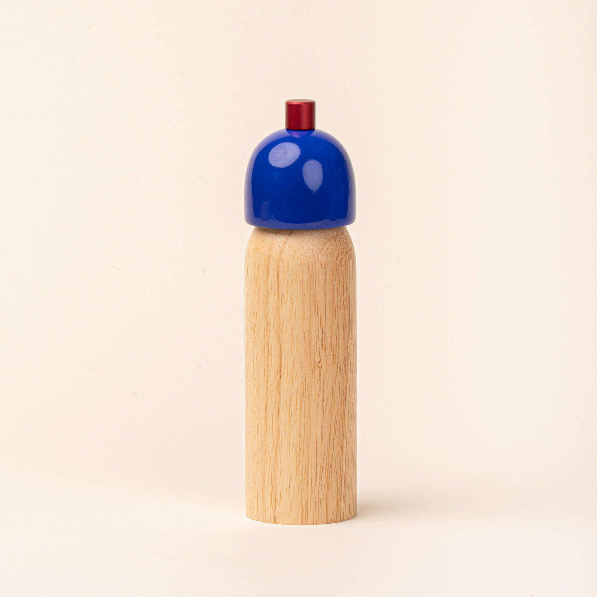 Wooden salt mill with a glossy cobalt-blue top and red knob, photographed against a warm cream background.
