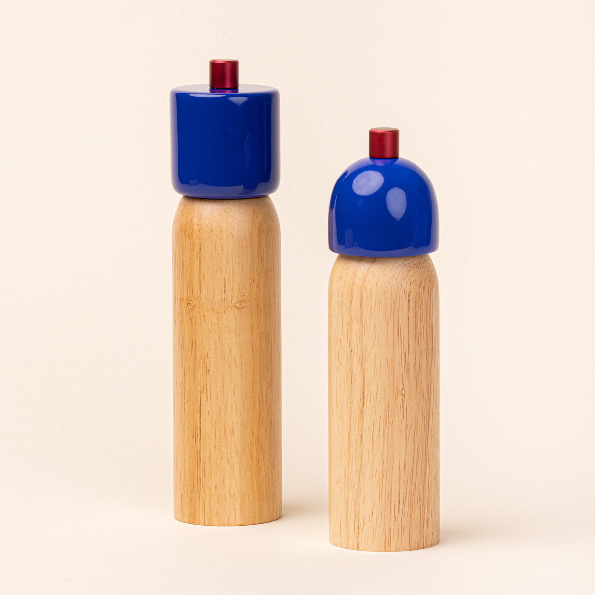 A wooden salt and pepper mill, each with a glossy cobalt-blue top and red knob, photographed against a warm cream background.