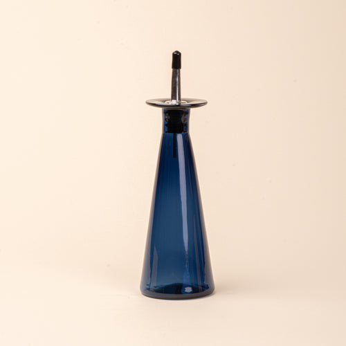A blue glass oil or vinegar dispenser with a tapered bottle shape, wide flared collar, and metal pour spout with a black stopper.