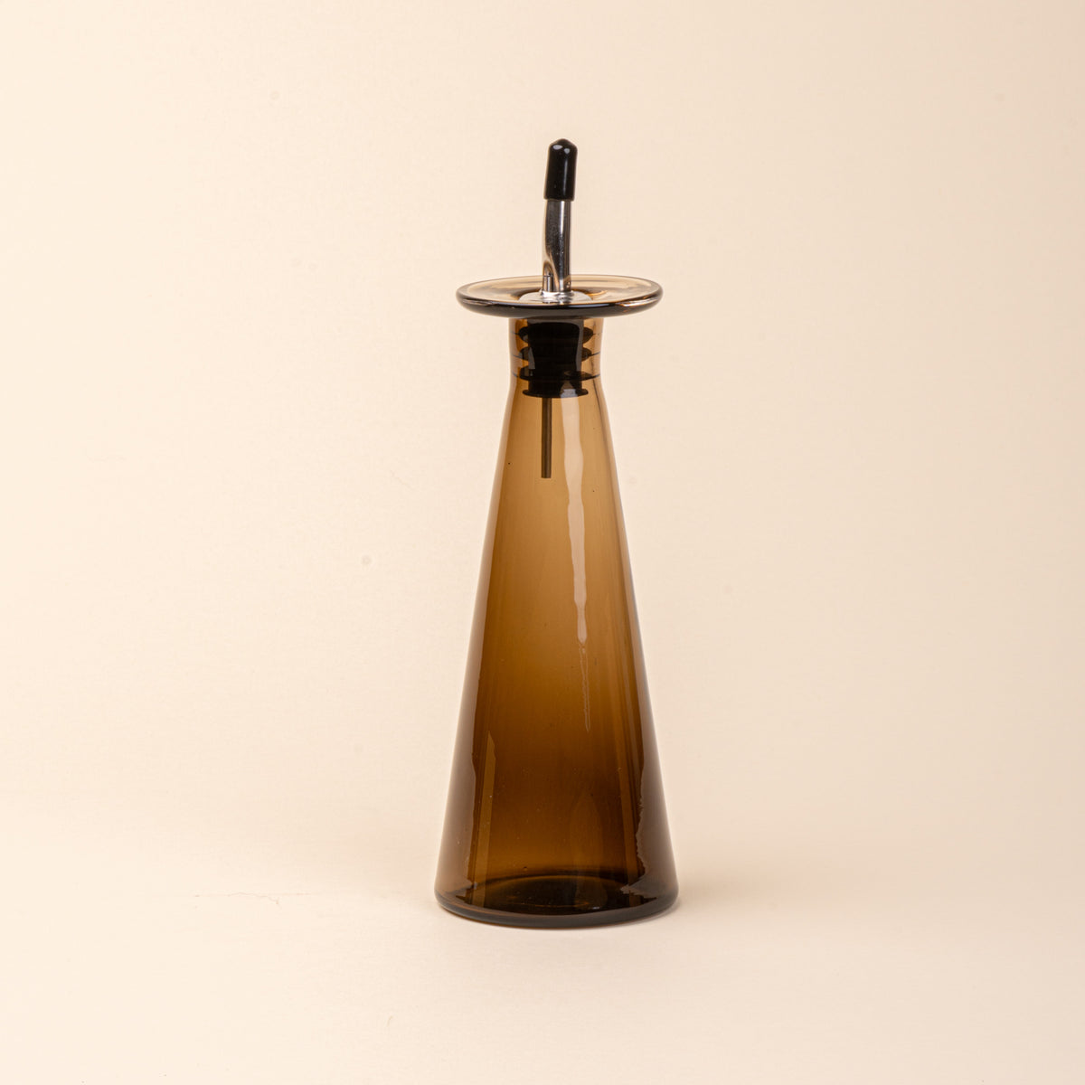 An amber-brown glass oil or vinegar dispenser with a tapered bottle shape, wide flared collar, and metal pour spout with a black stopper.