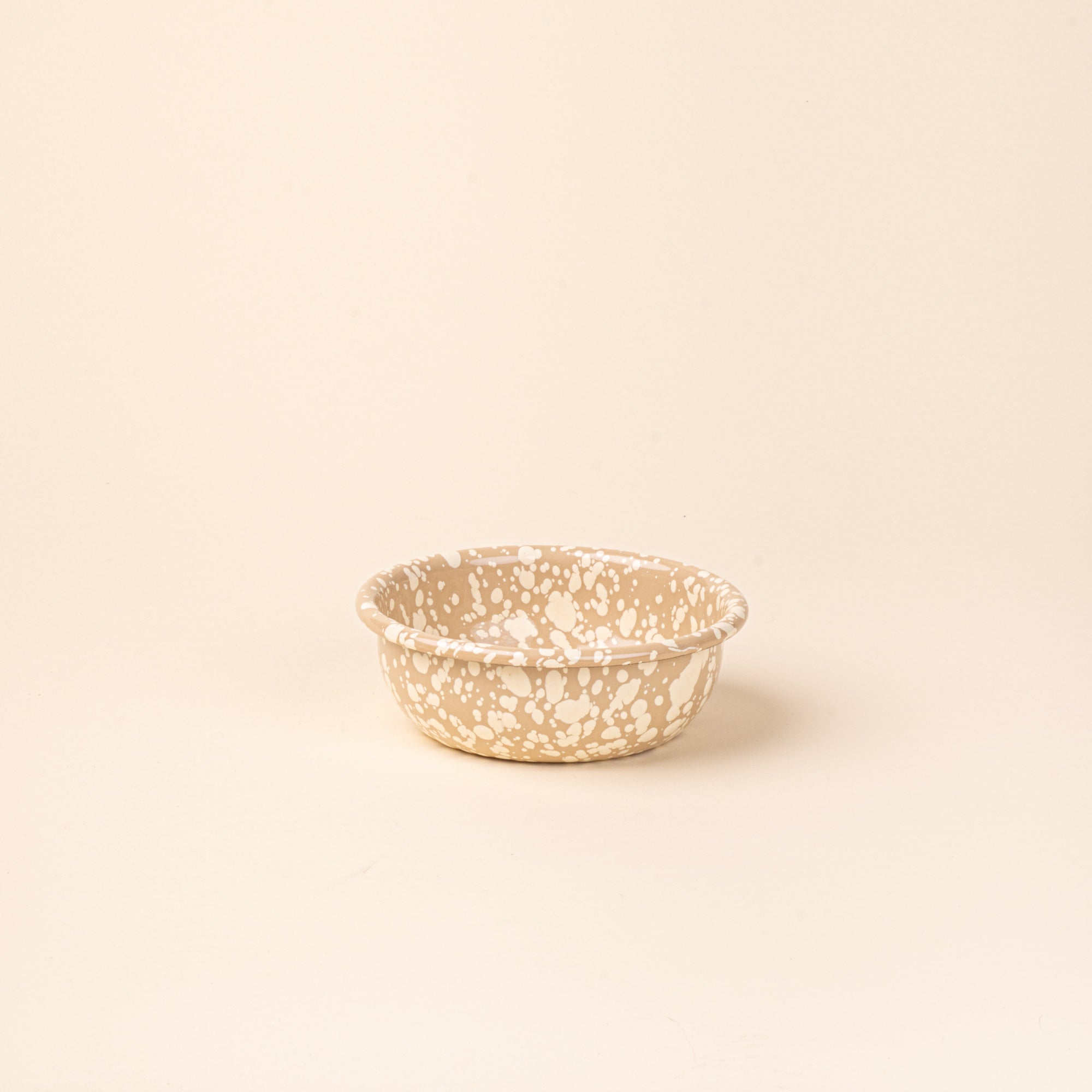 A small enamel bowl in neutral tan color with off-white splatter pattern.