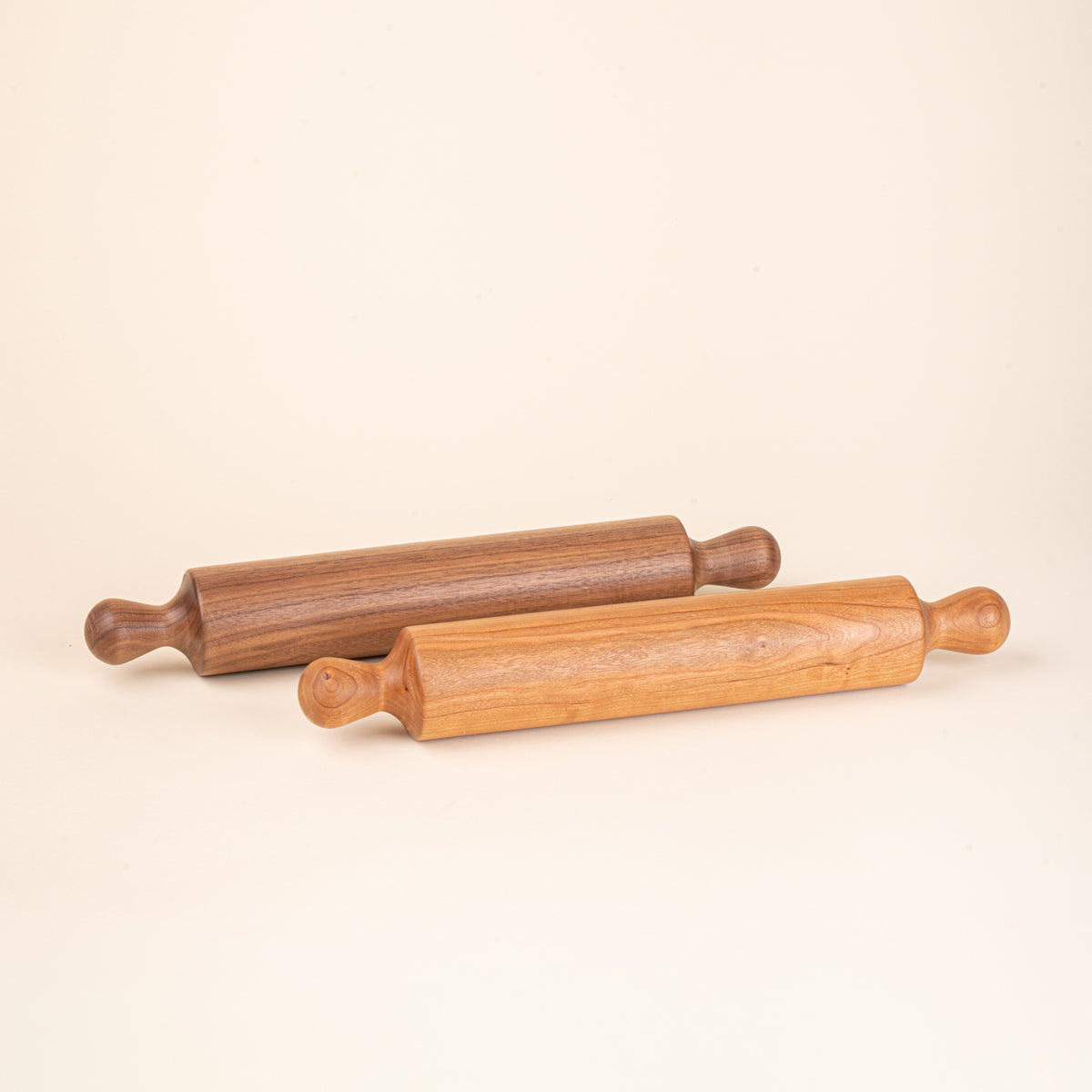 Two simple dowel wooden rolling pins with rounded handles, in walnut and cherry.