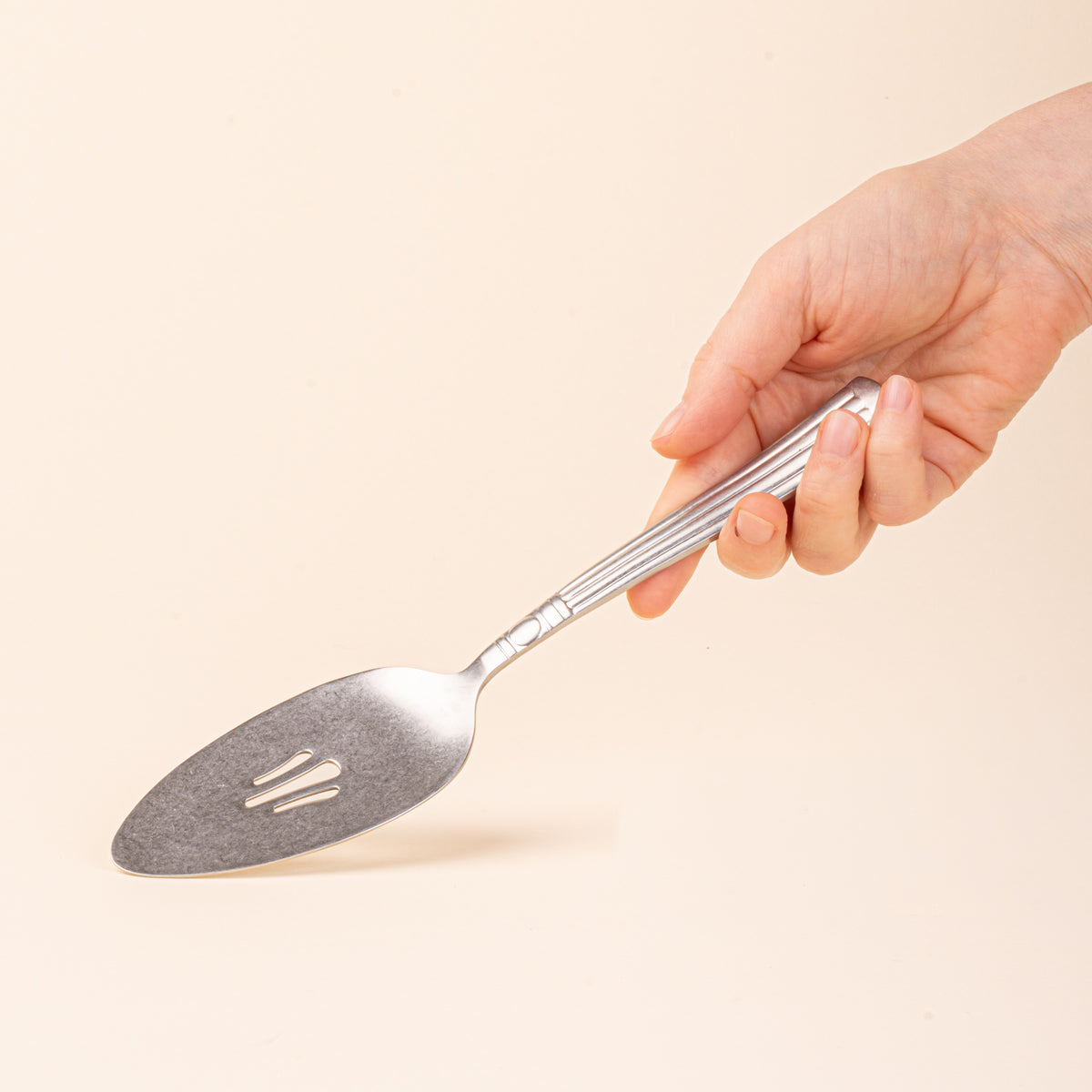 A hand holds a vintage-inspired silver pie server with a slotted blade and fluted handle.