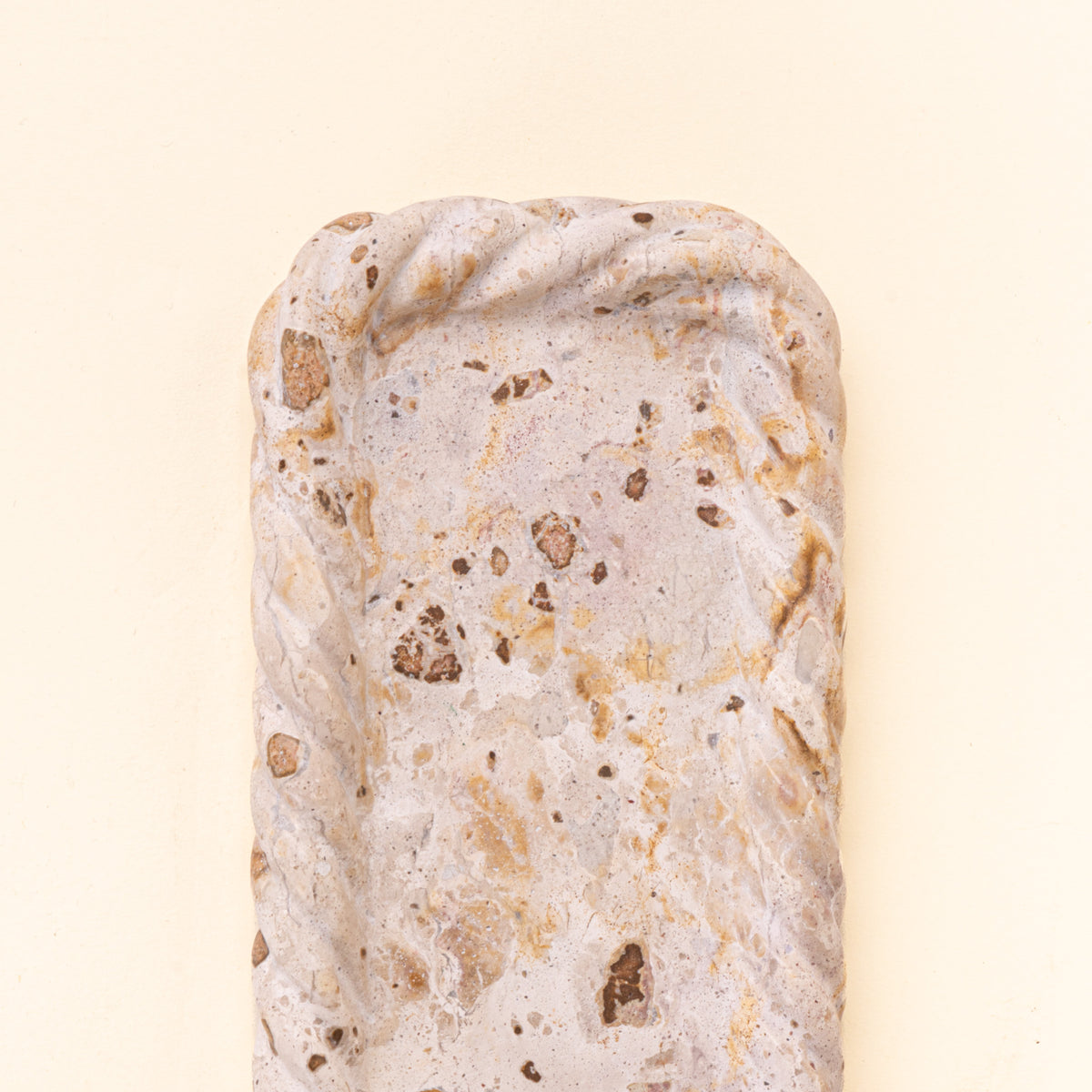 Closeup of a rectangular cream and brown speckled stone tray with a shallow recessed center and irregular scalloped edges.