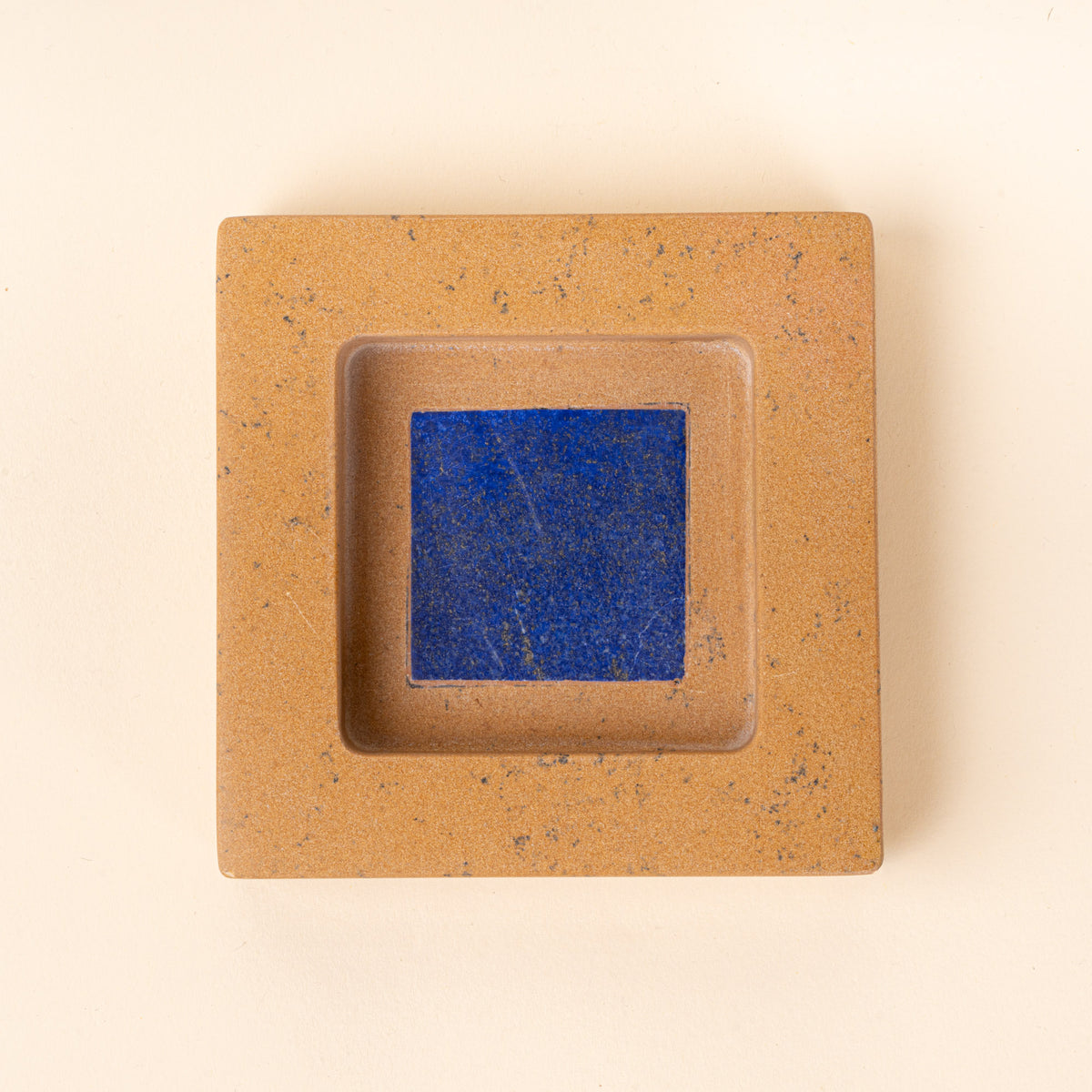 Overhead view of a square tan speckled jewelry dish with a recessed center and blue interior.