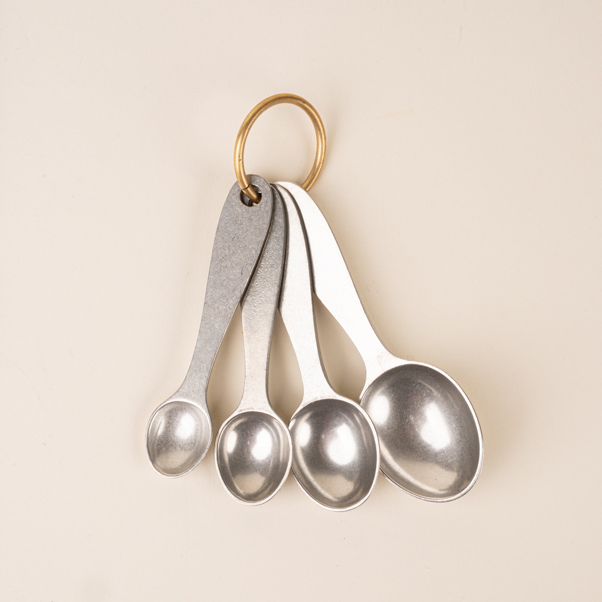 Four pewter measuring spoons on a brass ring.