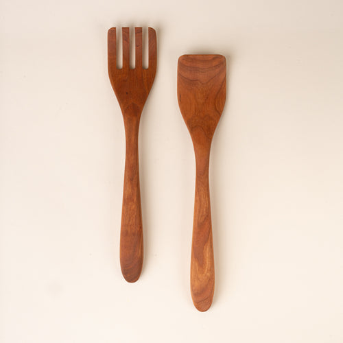 Two cherry wood kitchen utensils, a slotted spatula and a solid spatula, displayed side-by-side on a plain off-white background.