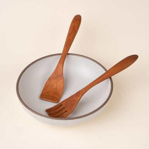 Two cherry wood kitchen utensils, a slotted spatula and a solid spatula, sitting in a ceramic serving bowl.
