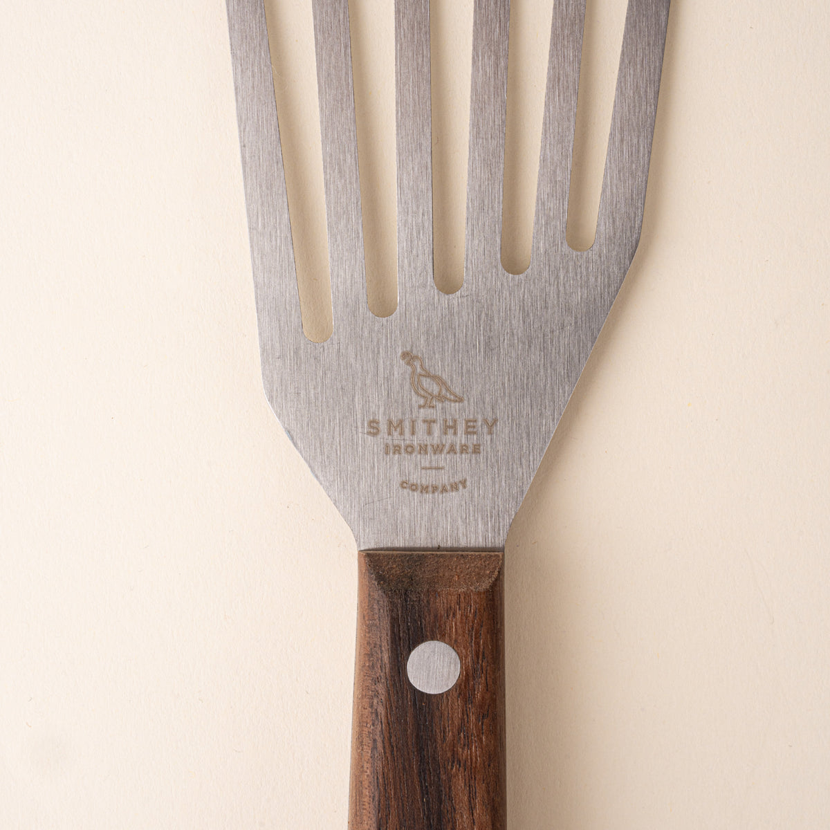 Closeup of the Smithey stamp on slotted stainless steel spatula with a wooden handle.