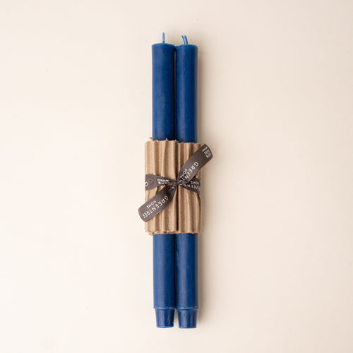 Two ultramarine taper candles bundled with corrugated cardboard and tied with a black ribbon on a neutral background.