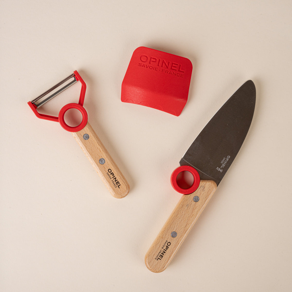 Kitchen tool set for children with a peeler, chef’s knife, and red scraper, each with red accents.