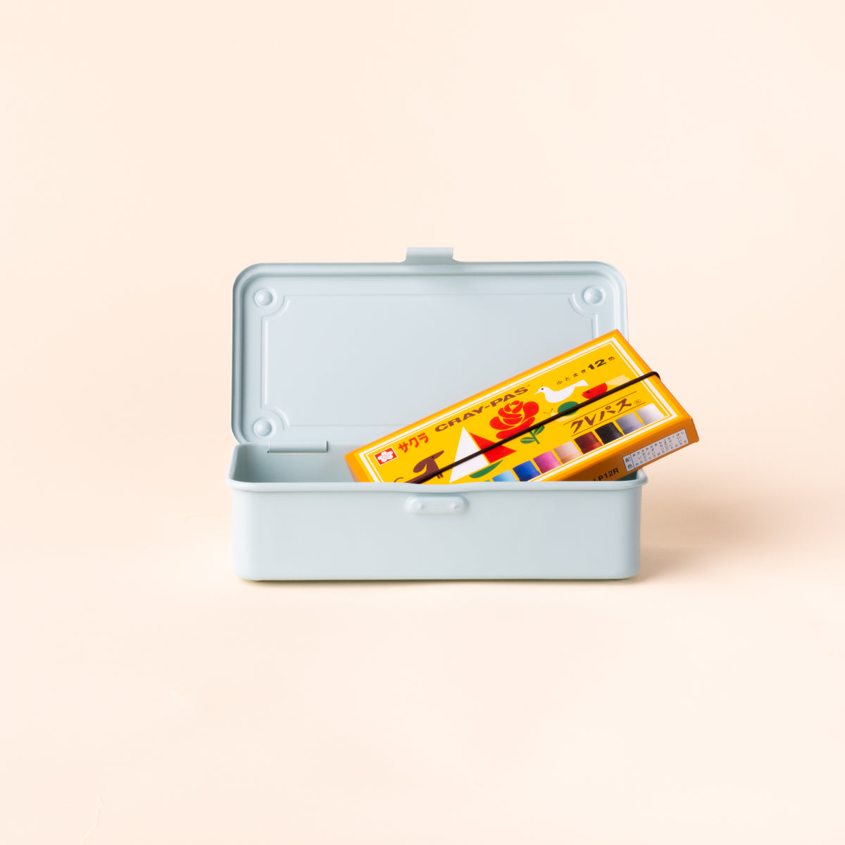 Open light blue rectangular storage box holding a yellow and orange box of crayons, with the hinged lid upright against a cream background.