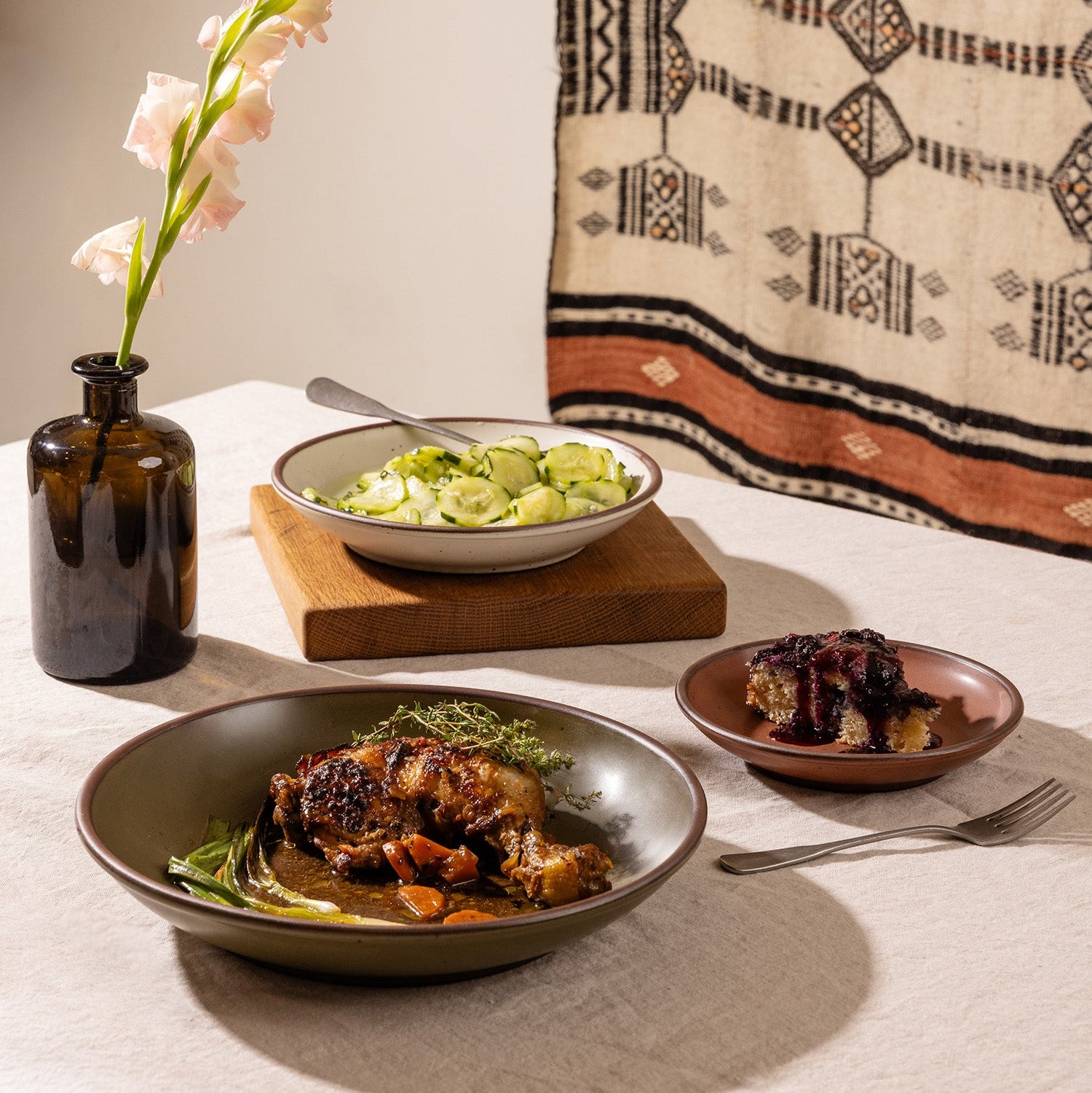 A styled dinner table scene with Little, Side and Dinner Coupes all with different dishes in each, witha. fork and vase of flowers.