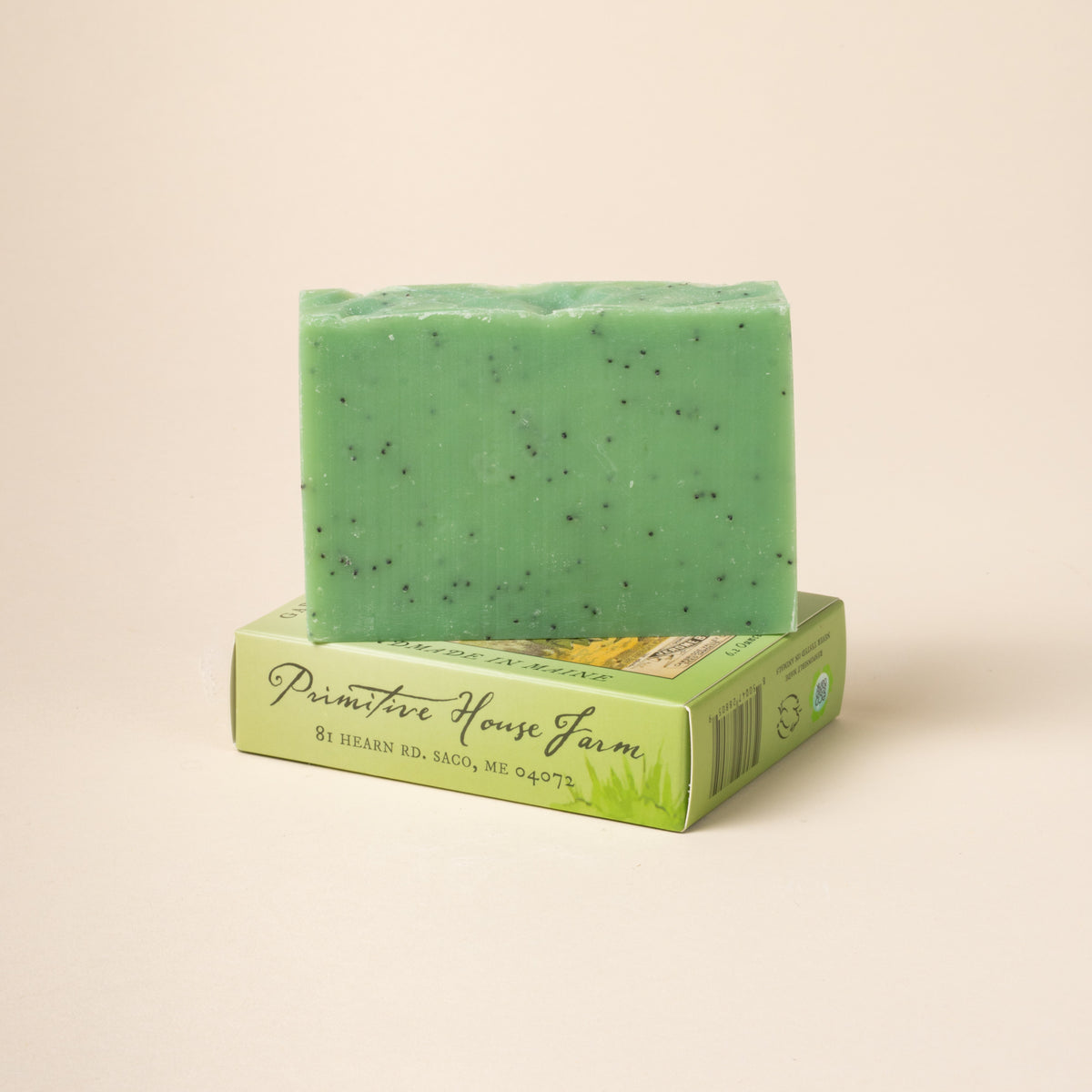 Green soap bar with specks on a matching box against a beige background