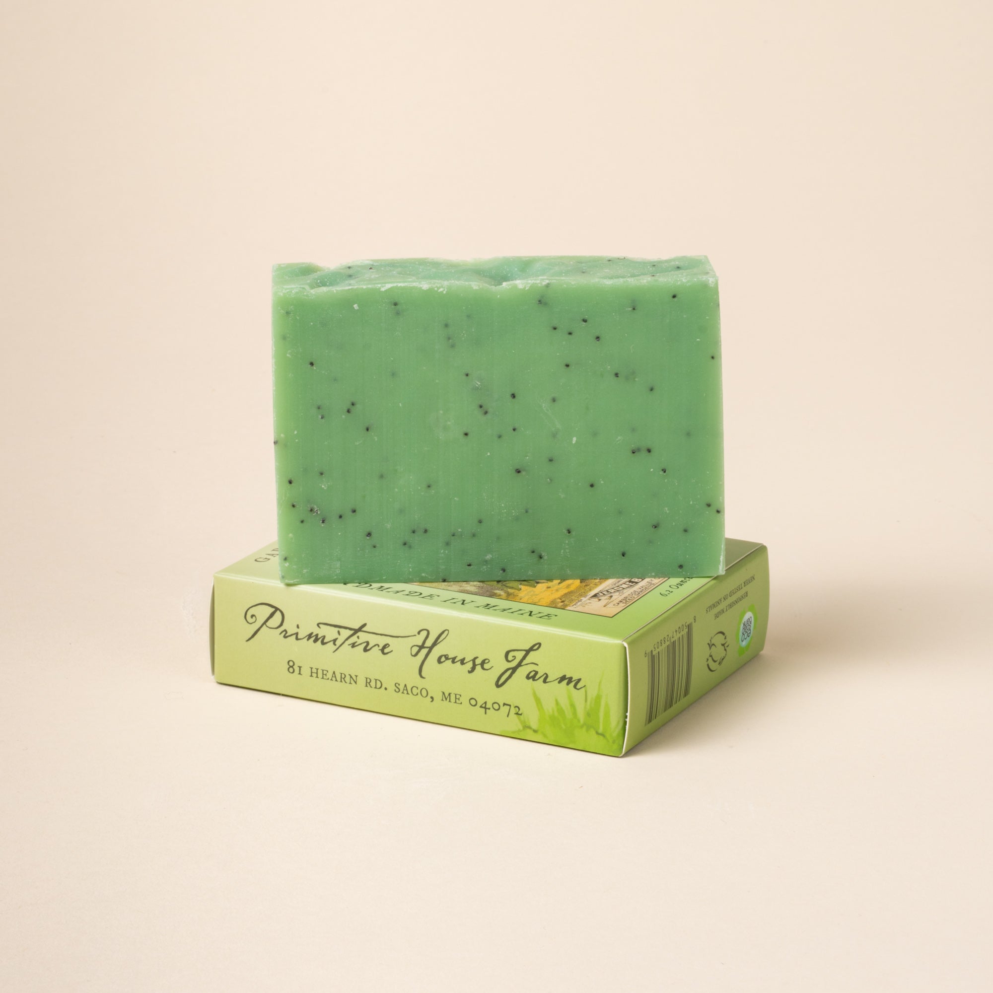 Green soap bar with specks on a matching box against a beige background