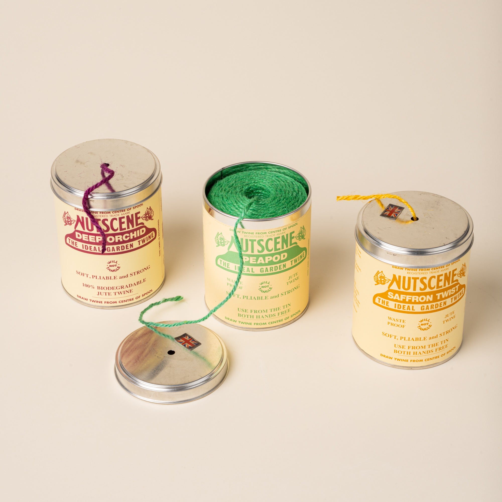 Three Nutscene garden twine tins, one open showing green twine, with loose lids and colored strands visible.