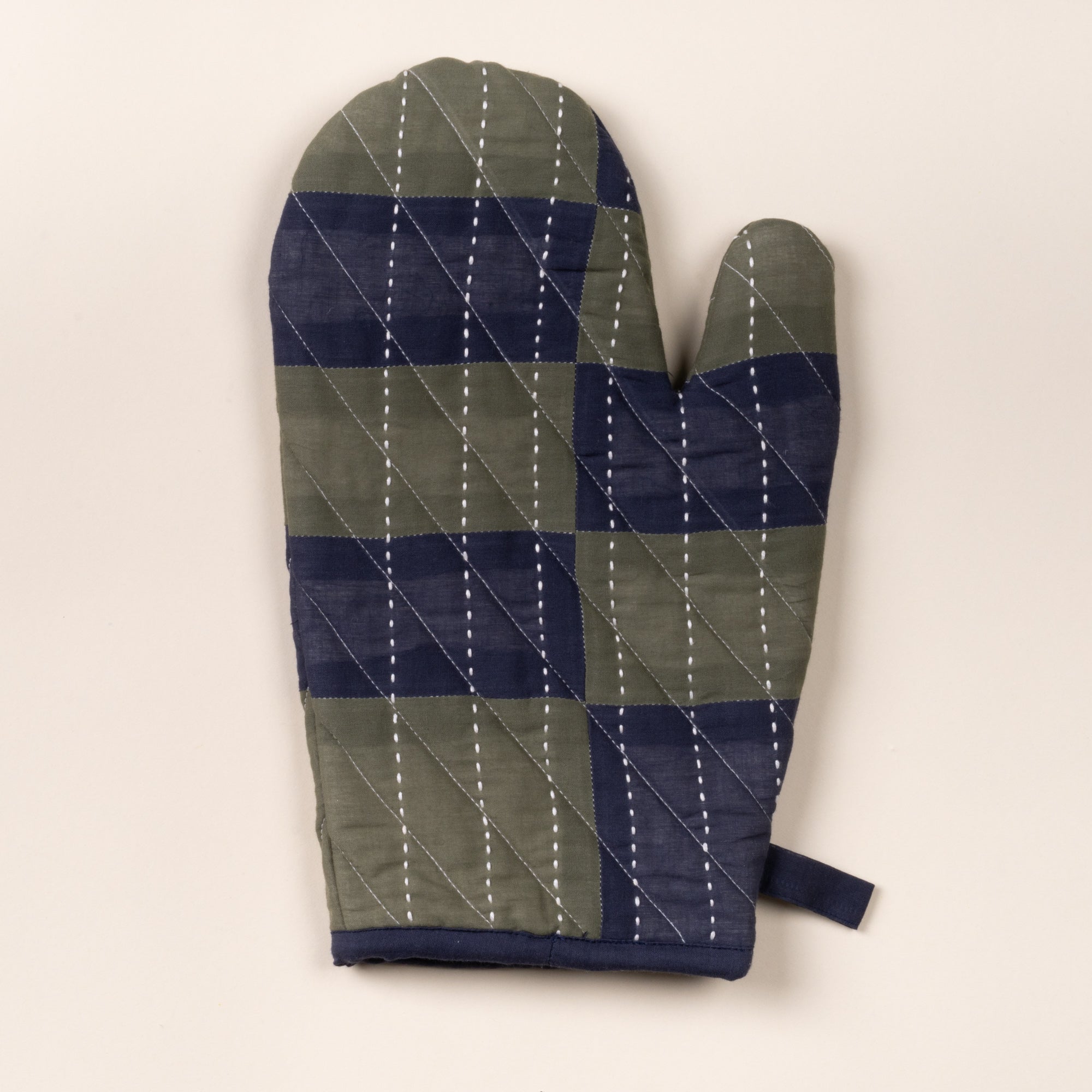 Quilted oven mitt with green and navy patchwork pattern and white stitched lines, shown on a neutral background.