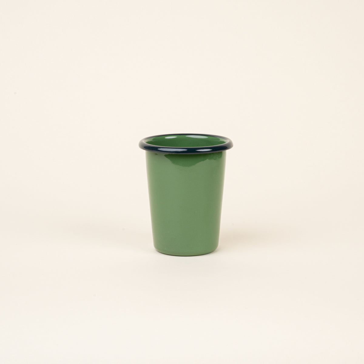 A short green enamel tumbler with a dark rim, set against a soft beige background.