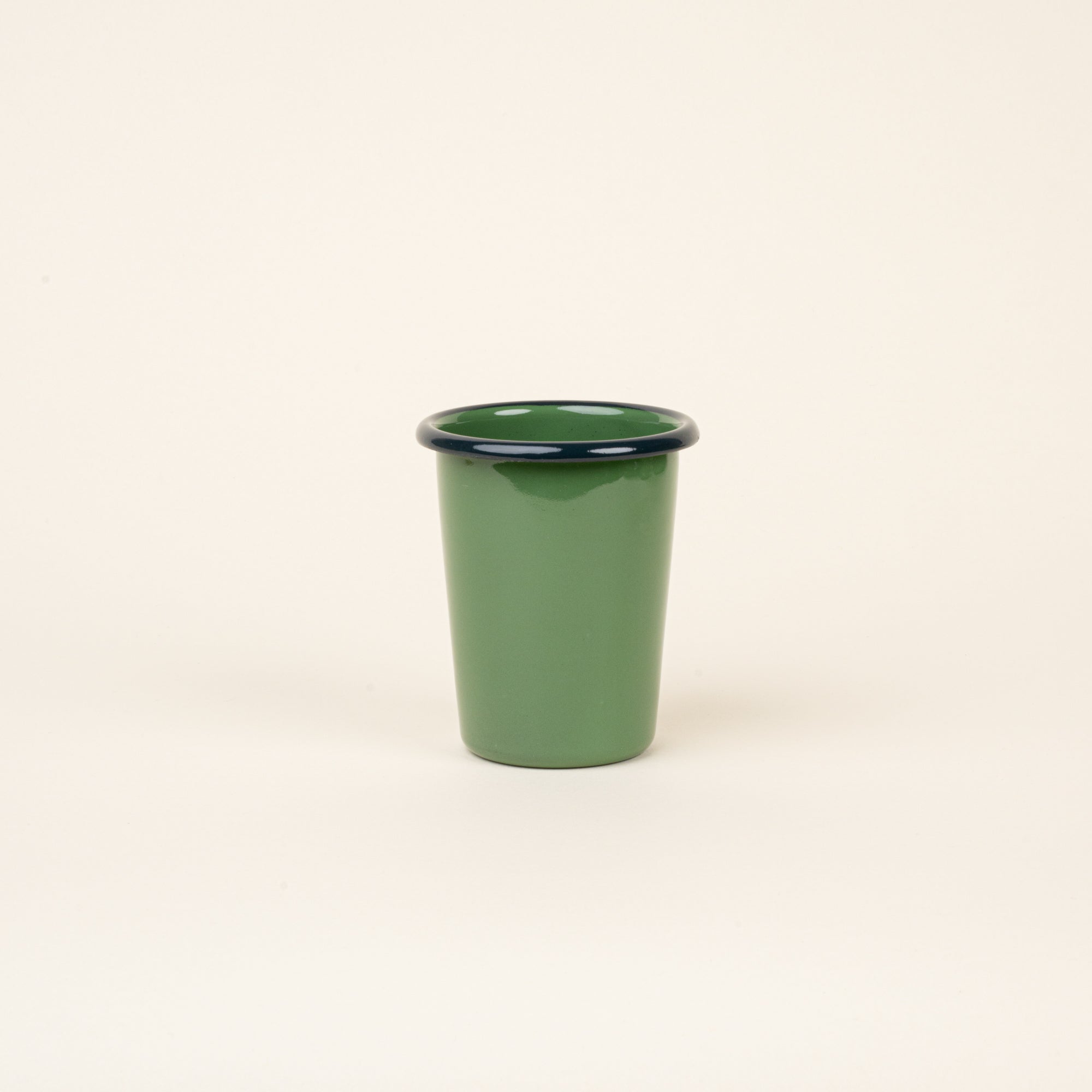 A short green enamel tumbler with a dark rim, set against a soft beige background.