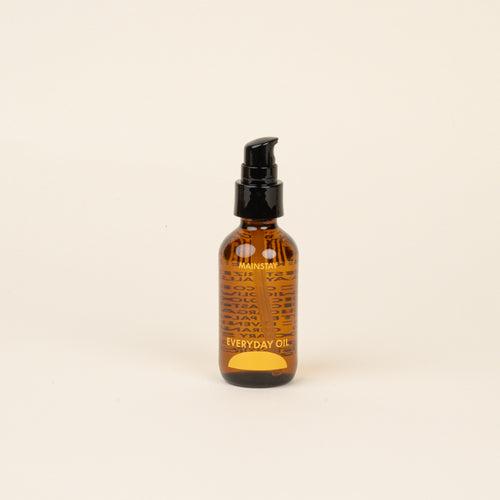 Amber glass bottle with black cap and label that reads 'Mainstay Everyday Oil' on a beige background.