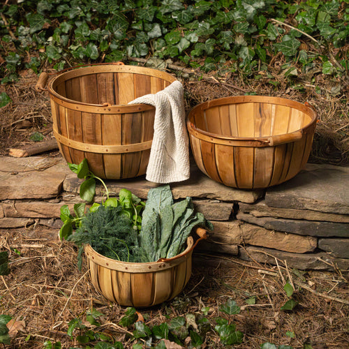 Three wooden baskets with plants and a towel on a stone surface with greenery in the background