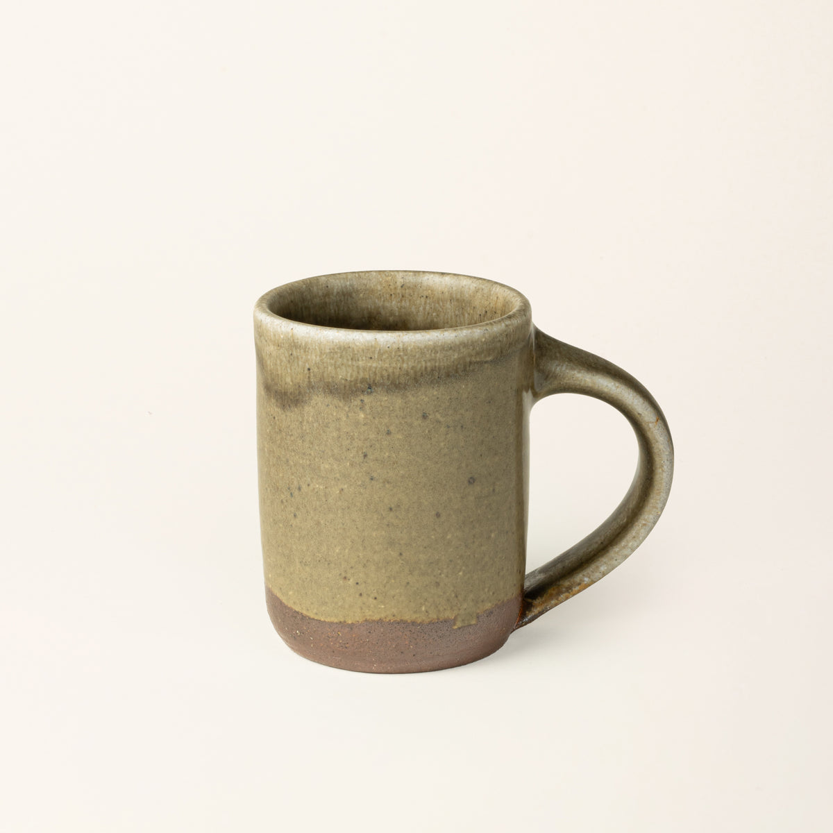 A handmade ceramic mug with a wood fired light earthy green glaze with an unglazed base.