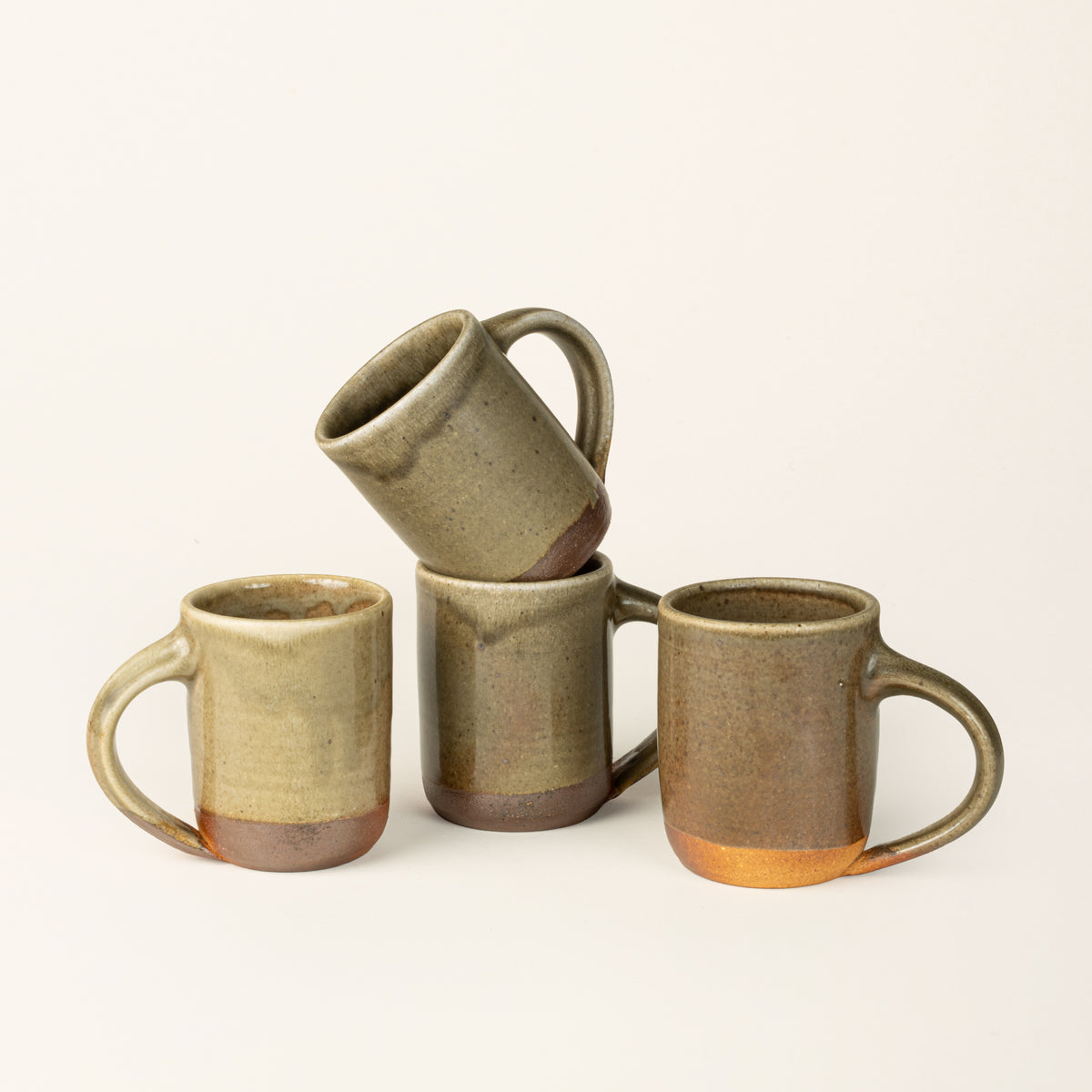 Four handmade ceramic mug with a wood fired light earthy green glaze with an unglazed base.